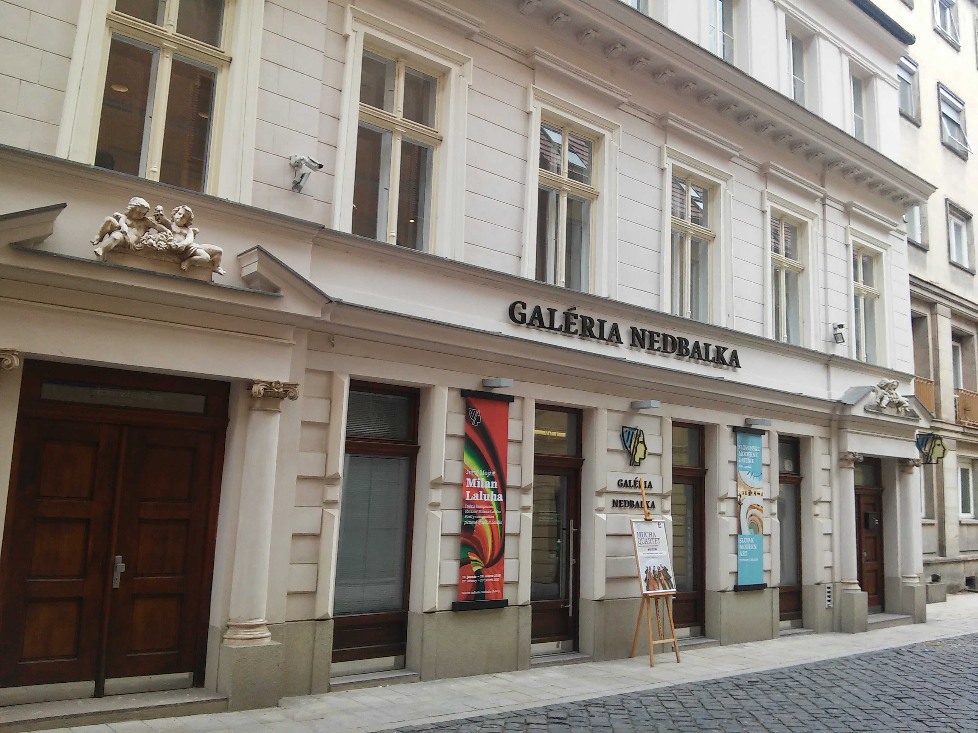 The Nedbalka Gallery facade on a cobbled street, with exhibition banners beside the entrance