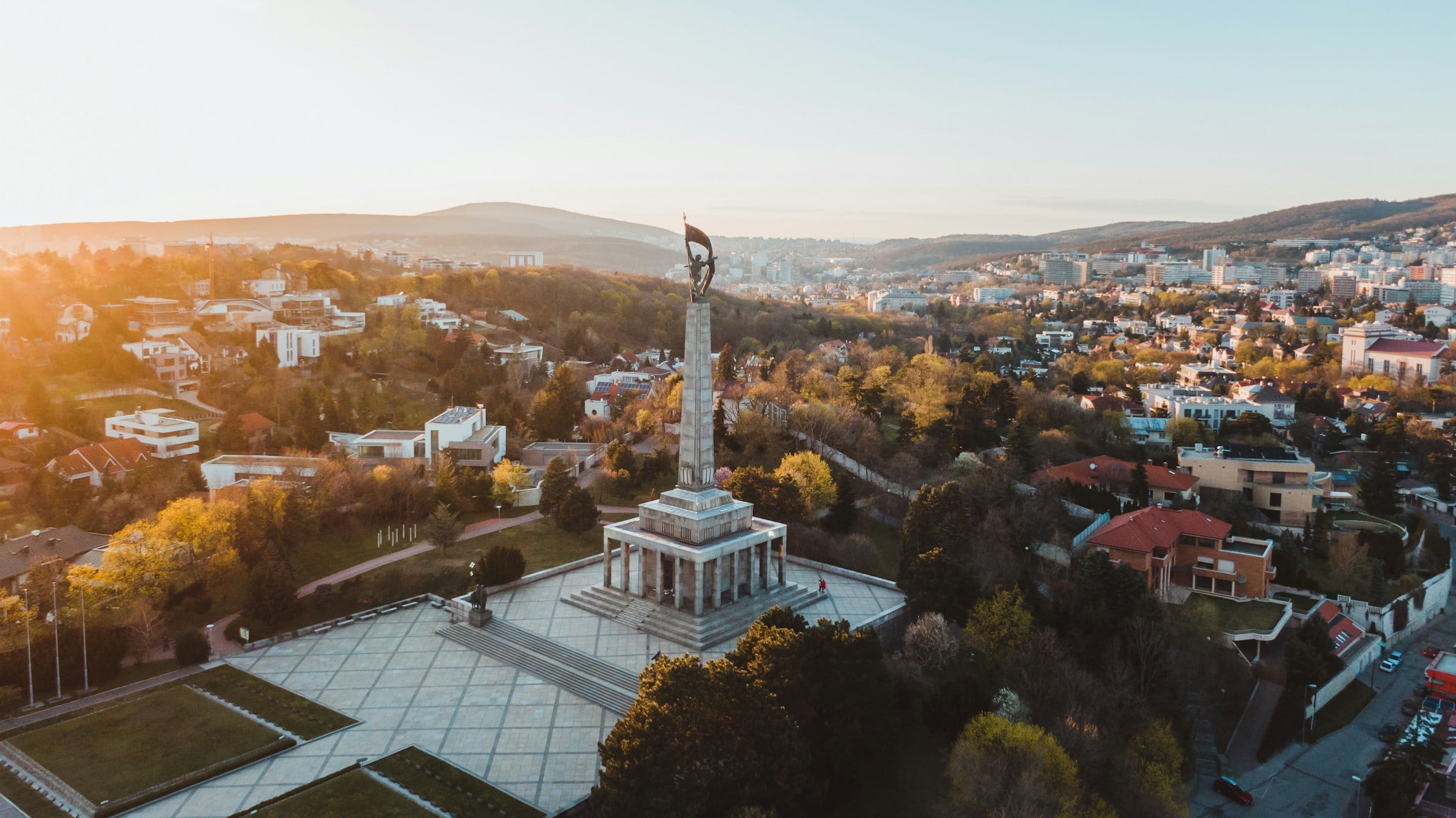 Aerial view of the Slavín memorial: a tall obelisk topped by a soldier raising a flag, above a colonnaded hall and a wide paved terrace