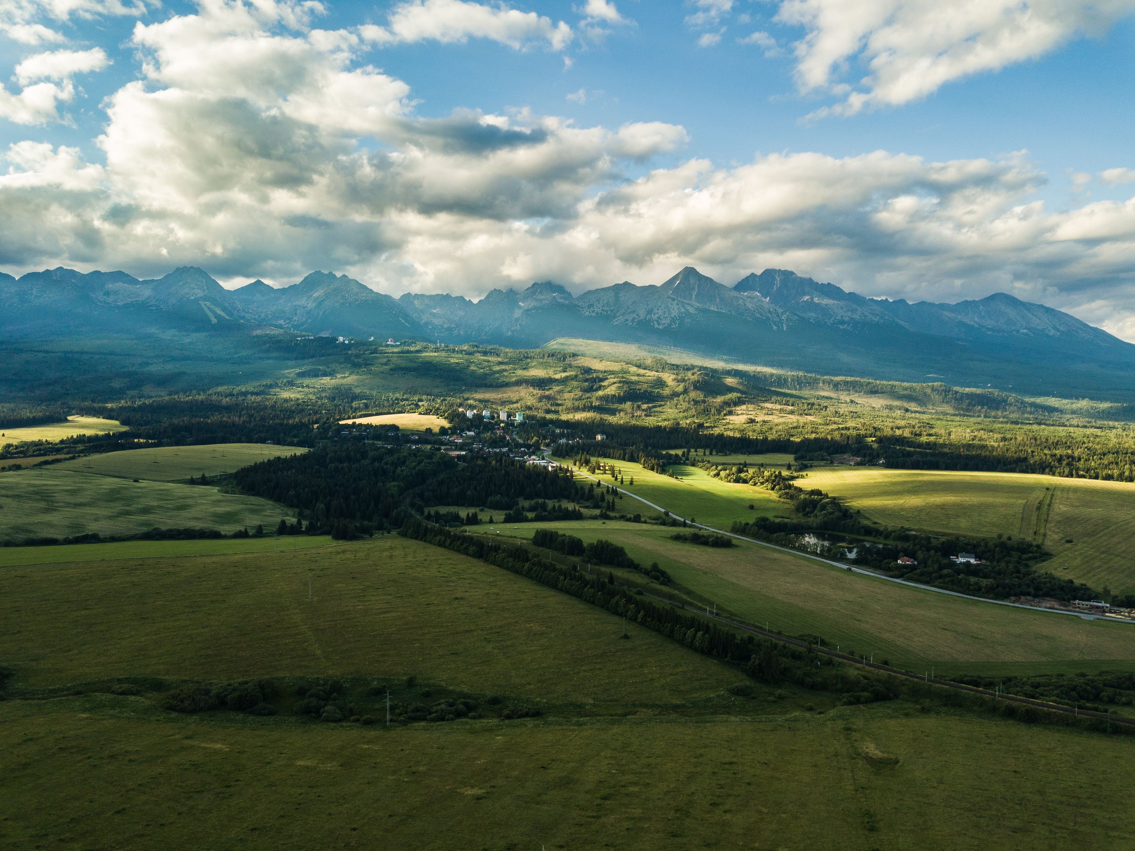 Aerial view of the High Tatras ridge above meadows, forest and a village in the valley
