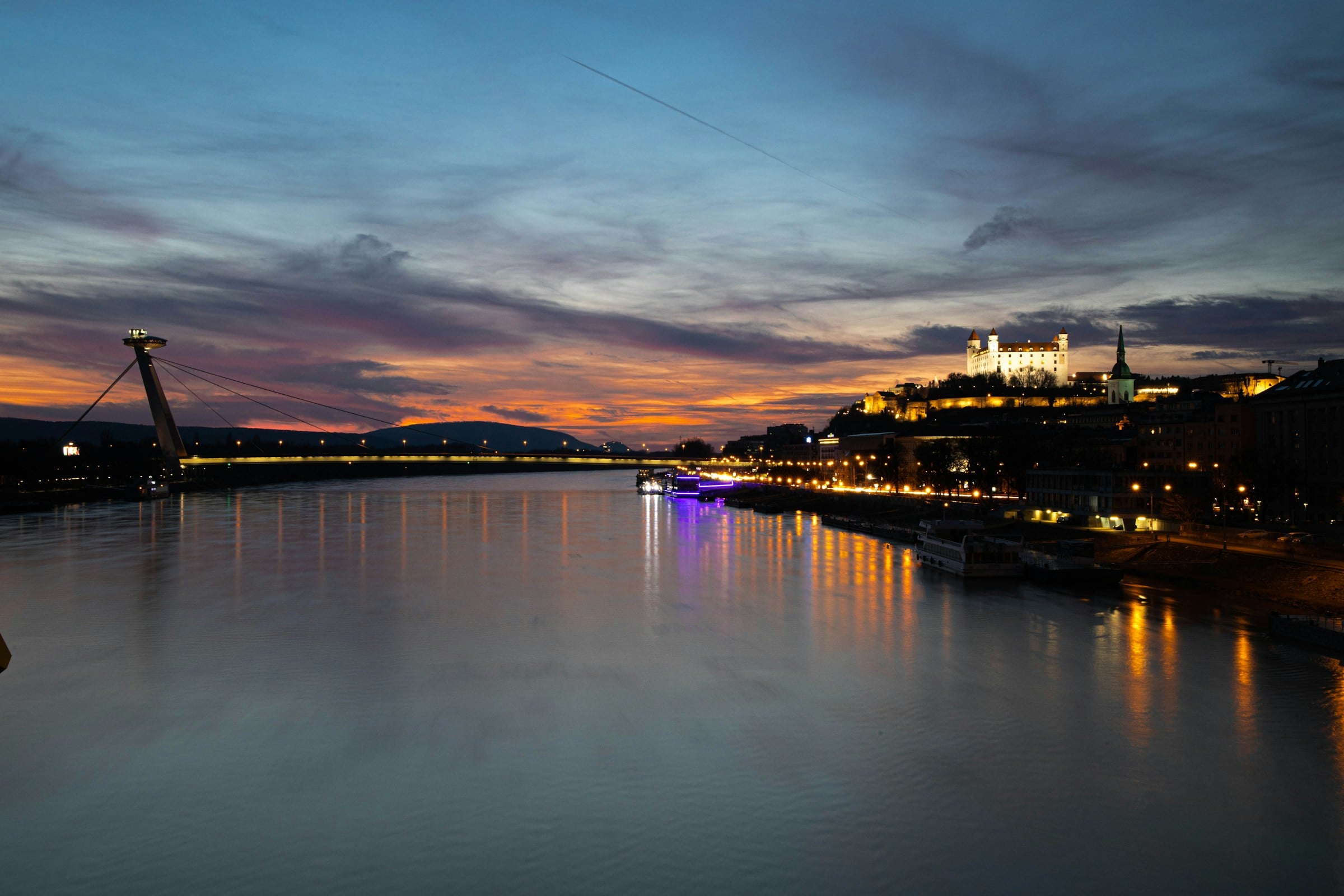 Sunset over the Danube seen from the Old Bridge, with city buildings glowing orange along the water