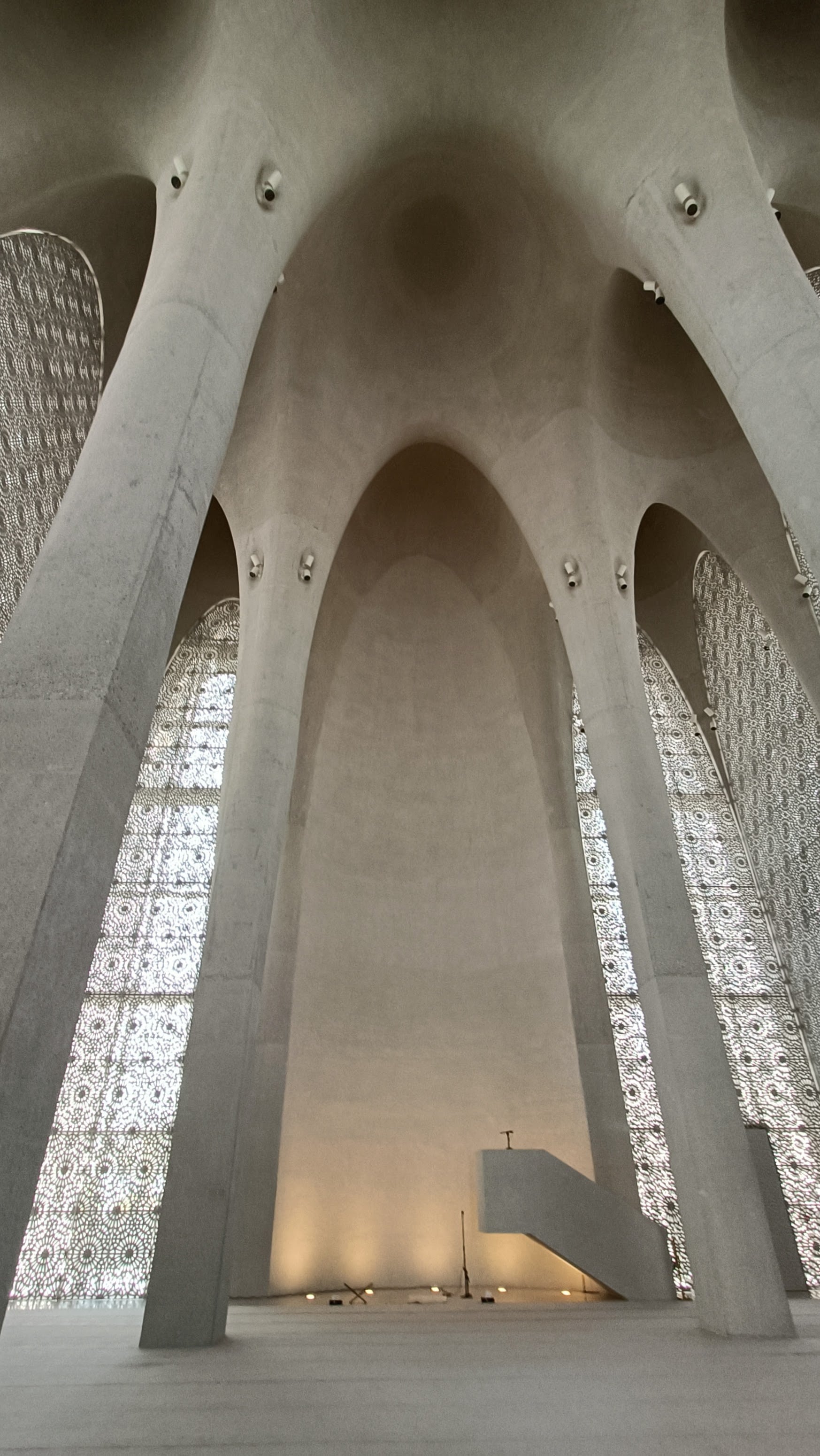 Interior of the mosque at the Abrahamic Family House: tall bare concrete arches meeting overhead, with light coming through patterned screens