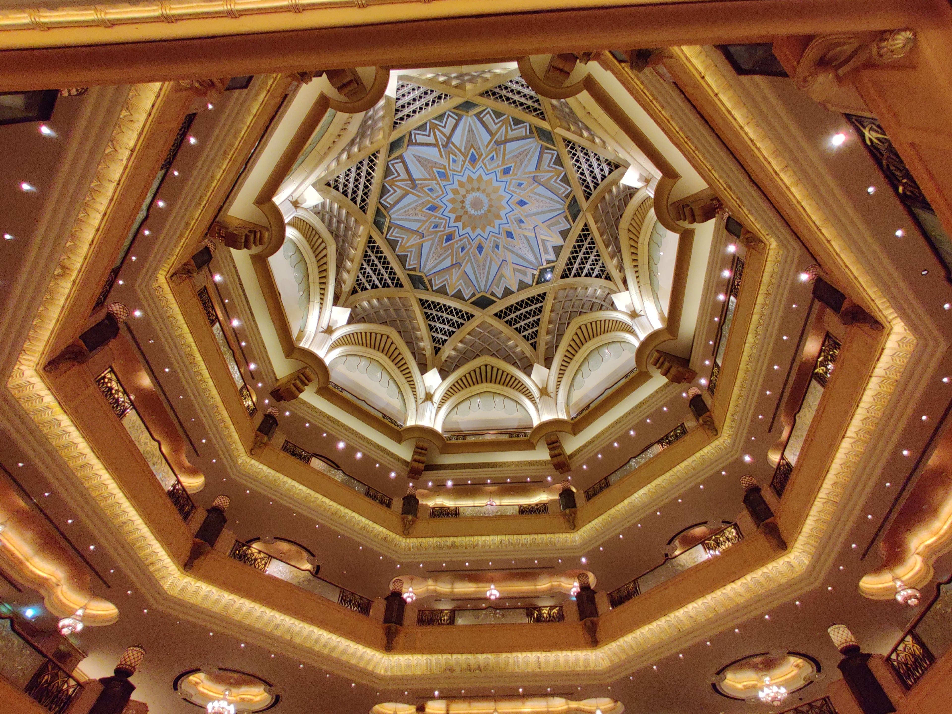 Ornate gold and patterned ceiling inside the Emirates Palace, with geometric Islamic ornamentation and a chandelier