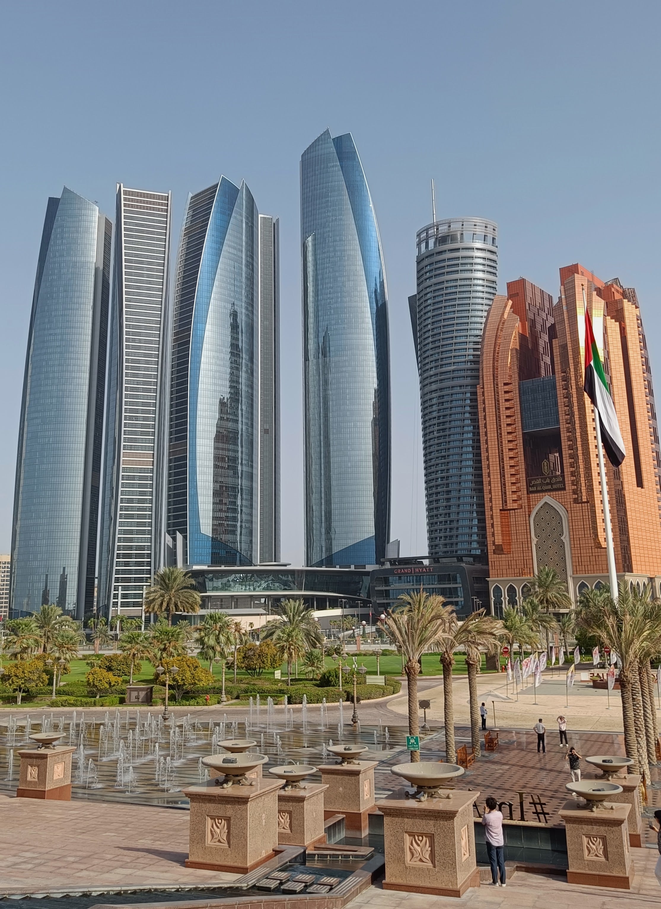 View from the steps of the Emirates Palace across fountains and palms to the curved glass Etihad Towers