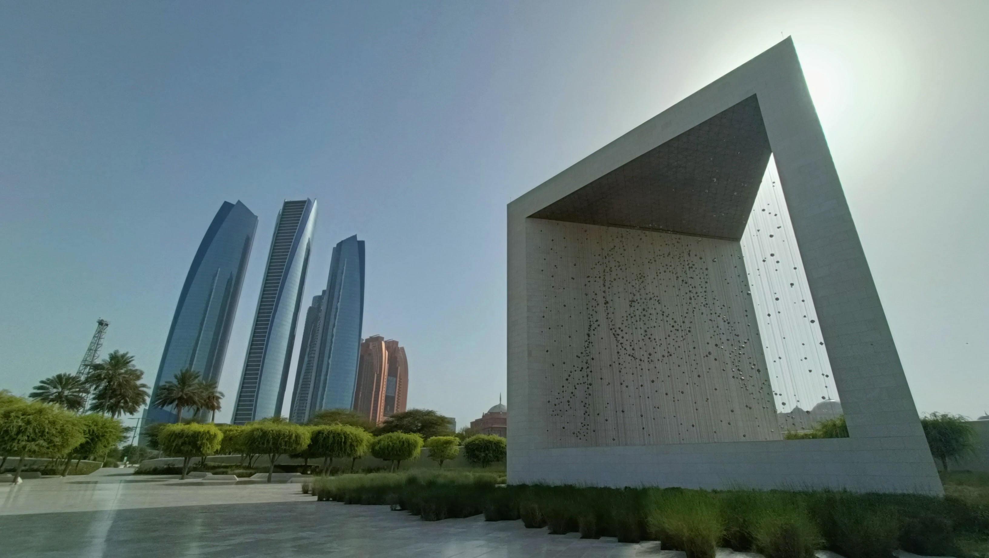 The Founder's Memorial: a huge open stone cube holding a suspended portrait made of over a thousand small shapes, with the Etihad Towers rising beyond the park