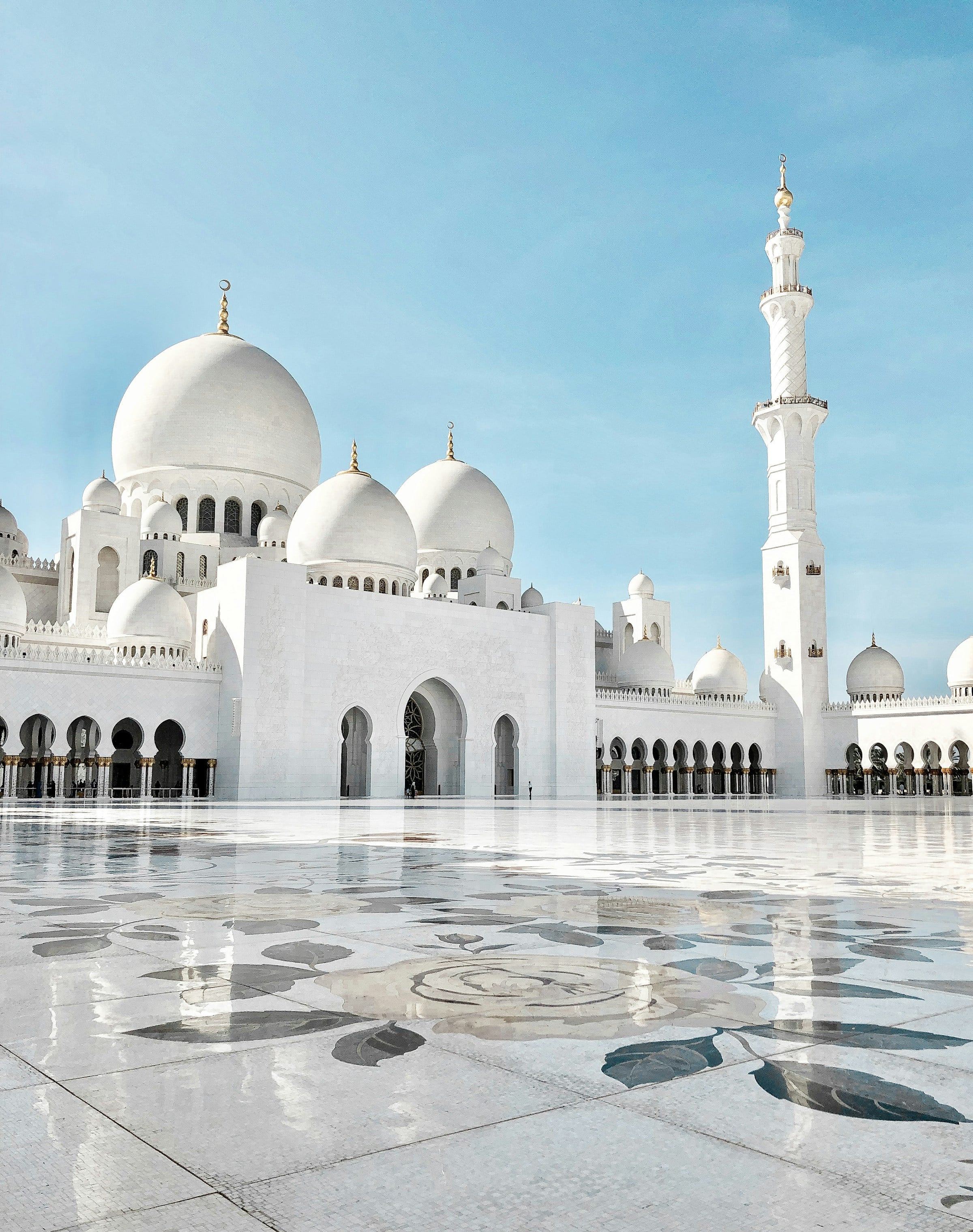 The white marble domes and minarets of the Sheikh Zayed Grand Mosque against a clear blue sky