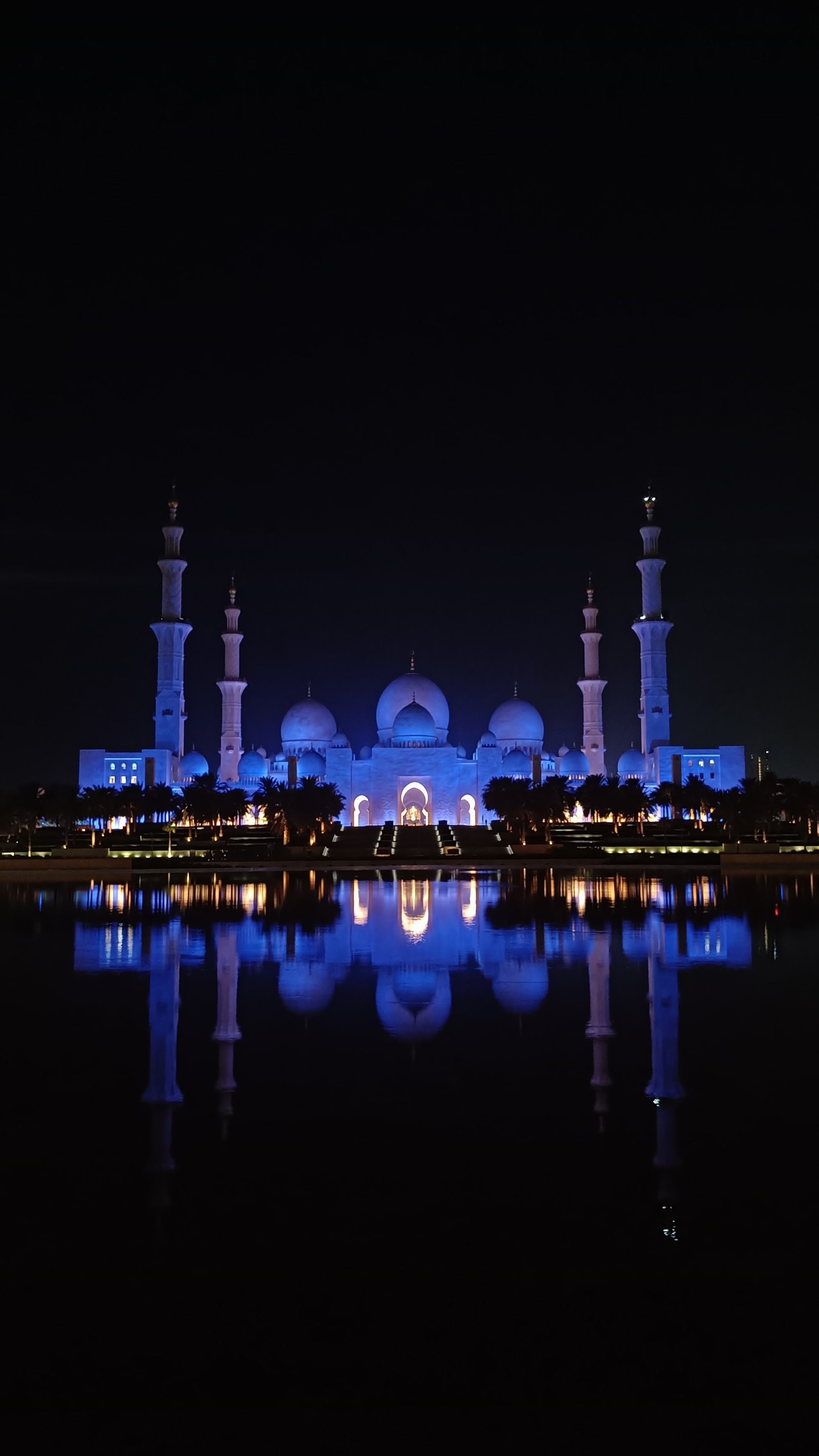 The Sheikh Zayed Grand Mosque lit in blue at night, mirrored in the still water of a lake in front of it