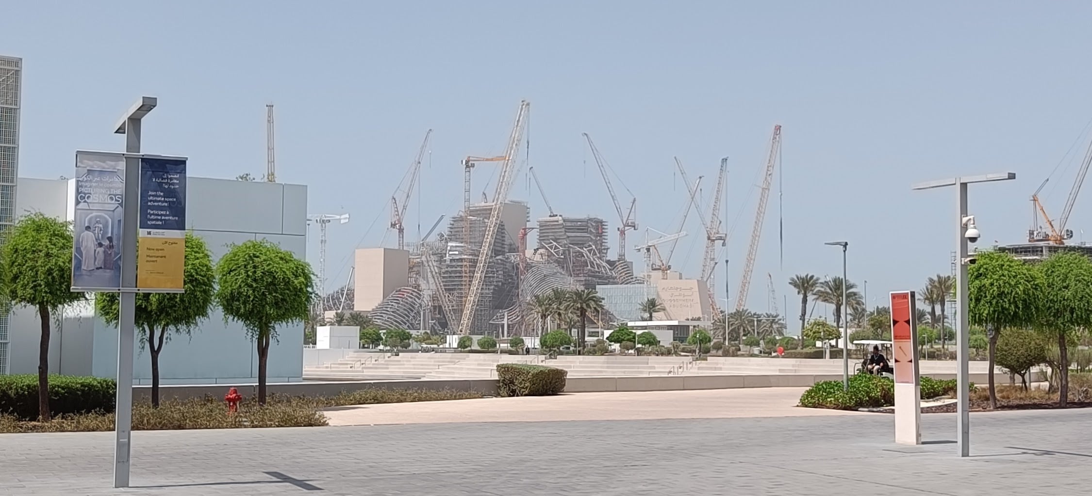 A wide empty plaza in the cultural district, with a forest of construction cranes over the half-built Guggenheim Abu Dhabi in the background