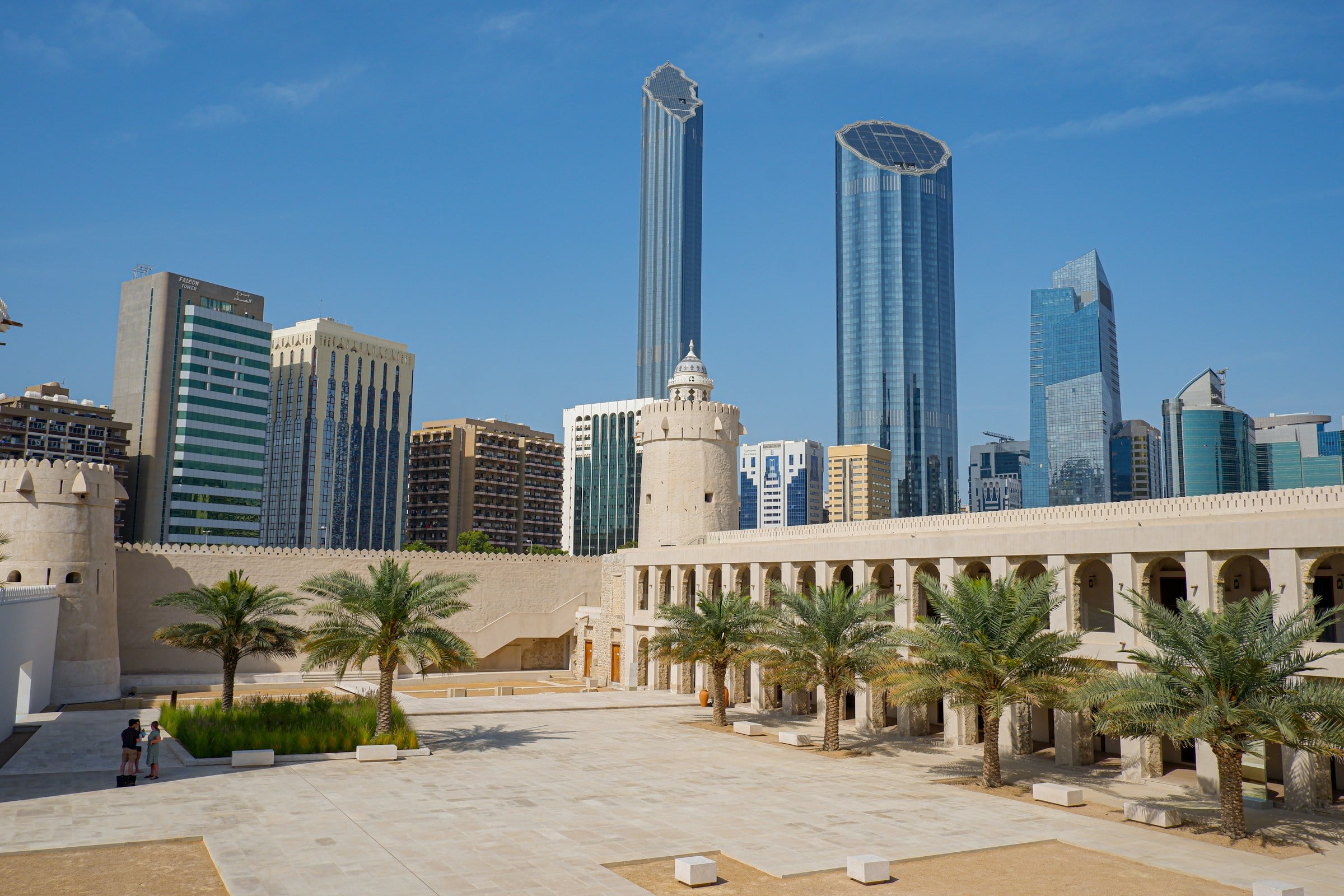 The pale walls, watchtower and palm-lined courtyard of Qasr Al Hosn fort, with the glass towers of downtown Abu Dhabi rising behind it