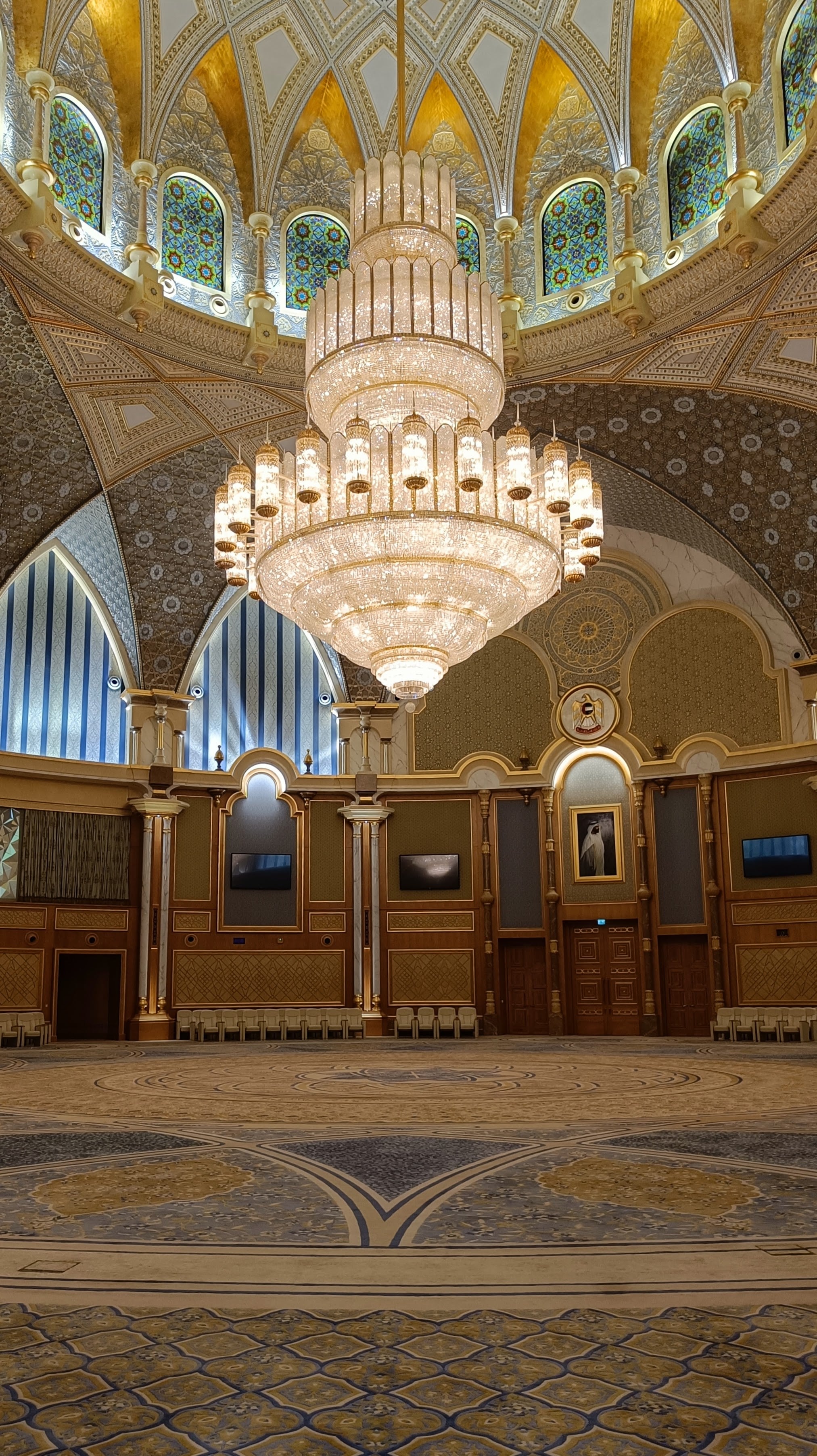 A council chamber in Qasr Al Watan with a huge crystal chandelier, patterned carpet and stained-glass windows around the dome